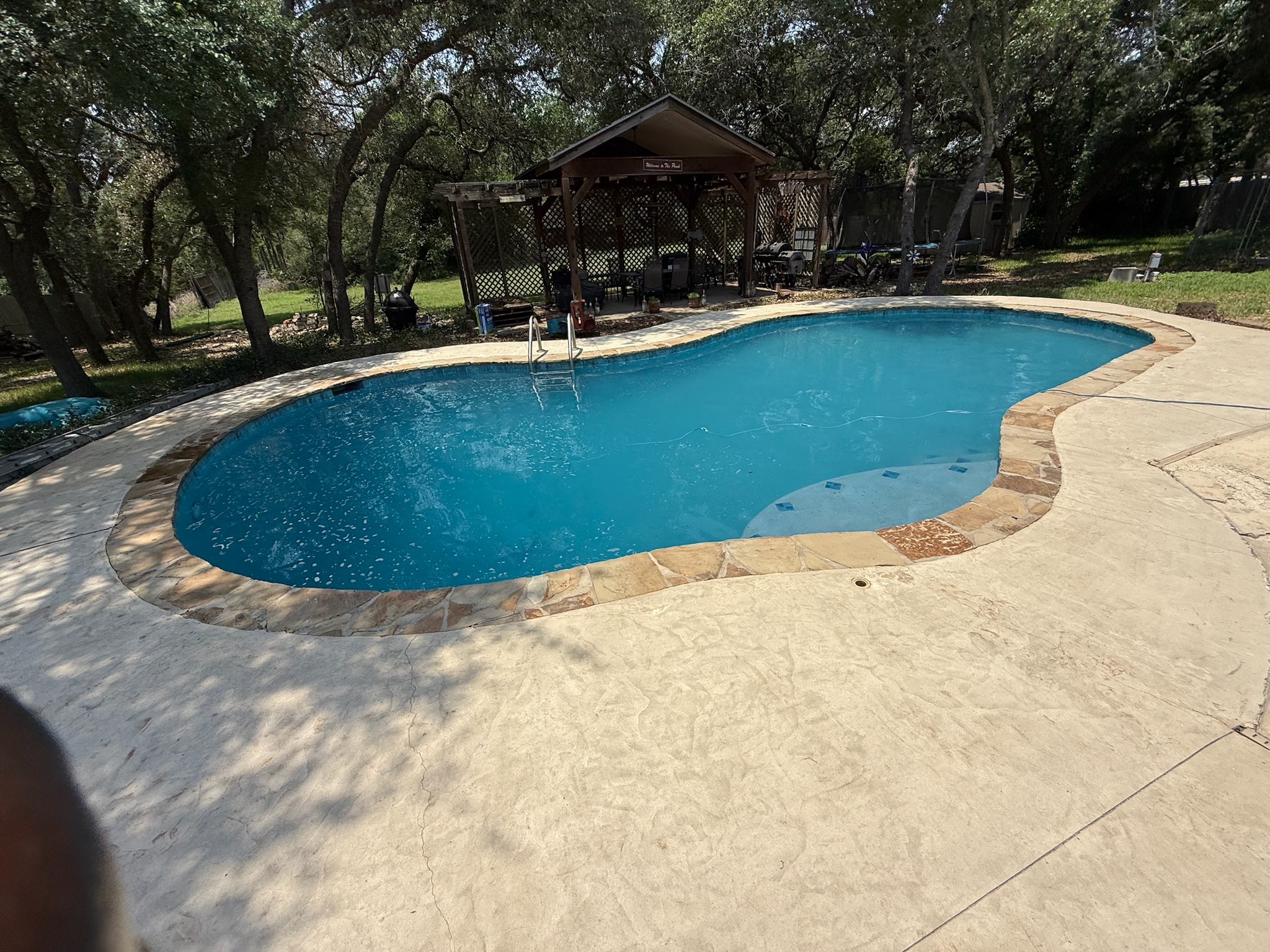 Completed tile and plaster remodel with the pool filled to normal water level, showing smooth light-blue plaster, new blue waterline tile and stone coping