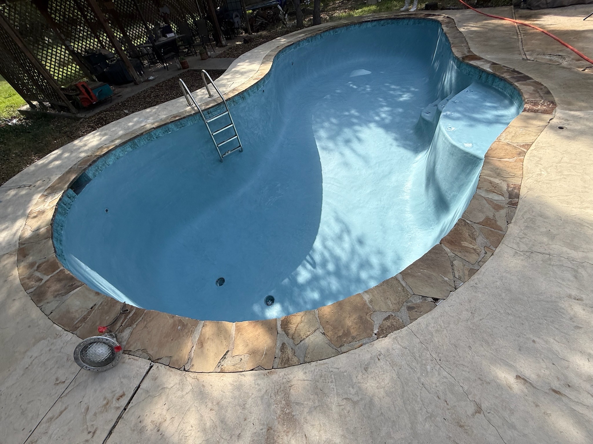 Empty pool with a fresh smooth light-blue plaster finish and new blue mosaic waterline tile, ready to be filled during a tile and plaster remodel