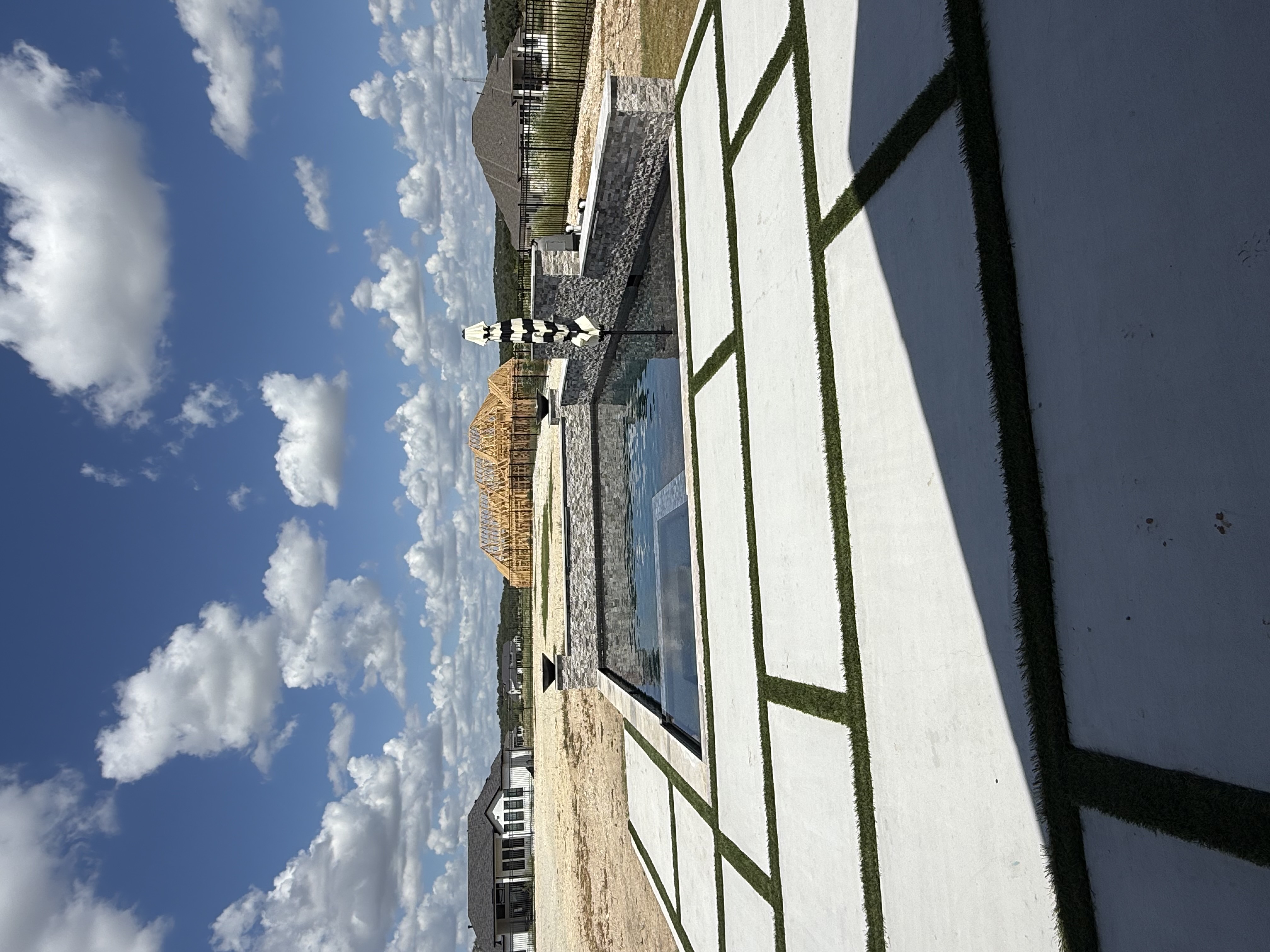 Boerne infinity-edge pool with a flush integrated spa, stacked-stone bond beam with accent lights, tanning ledge with striped umbrella and white geometric pavers