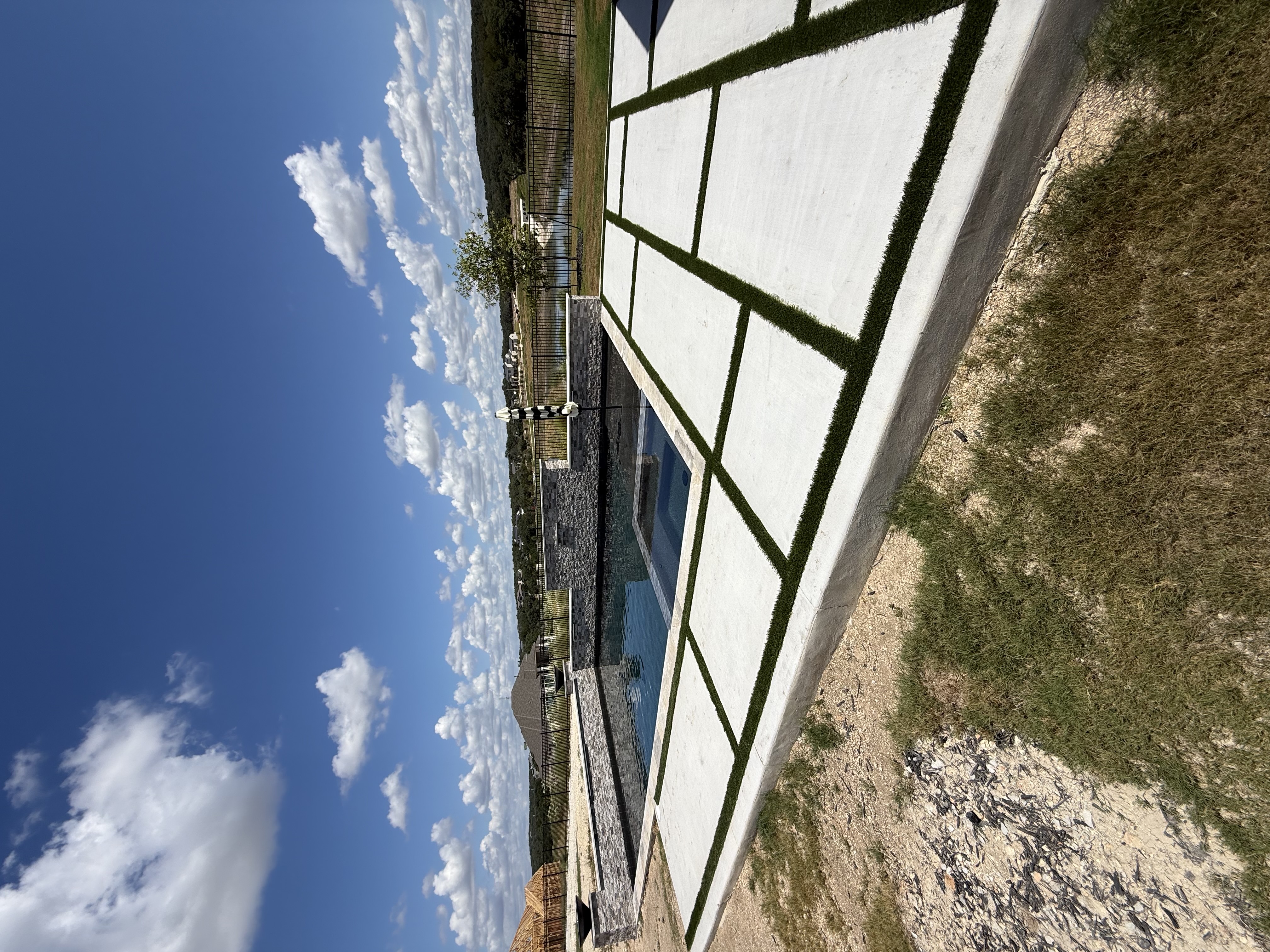 Boerne rectangular pool with a raised stacked-stone wall of water scuppers and accent lights beside white pavers in a turf grid