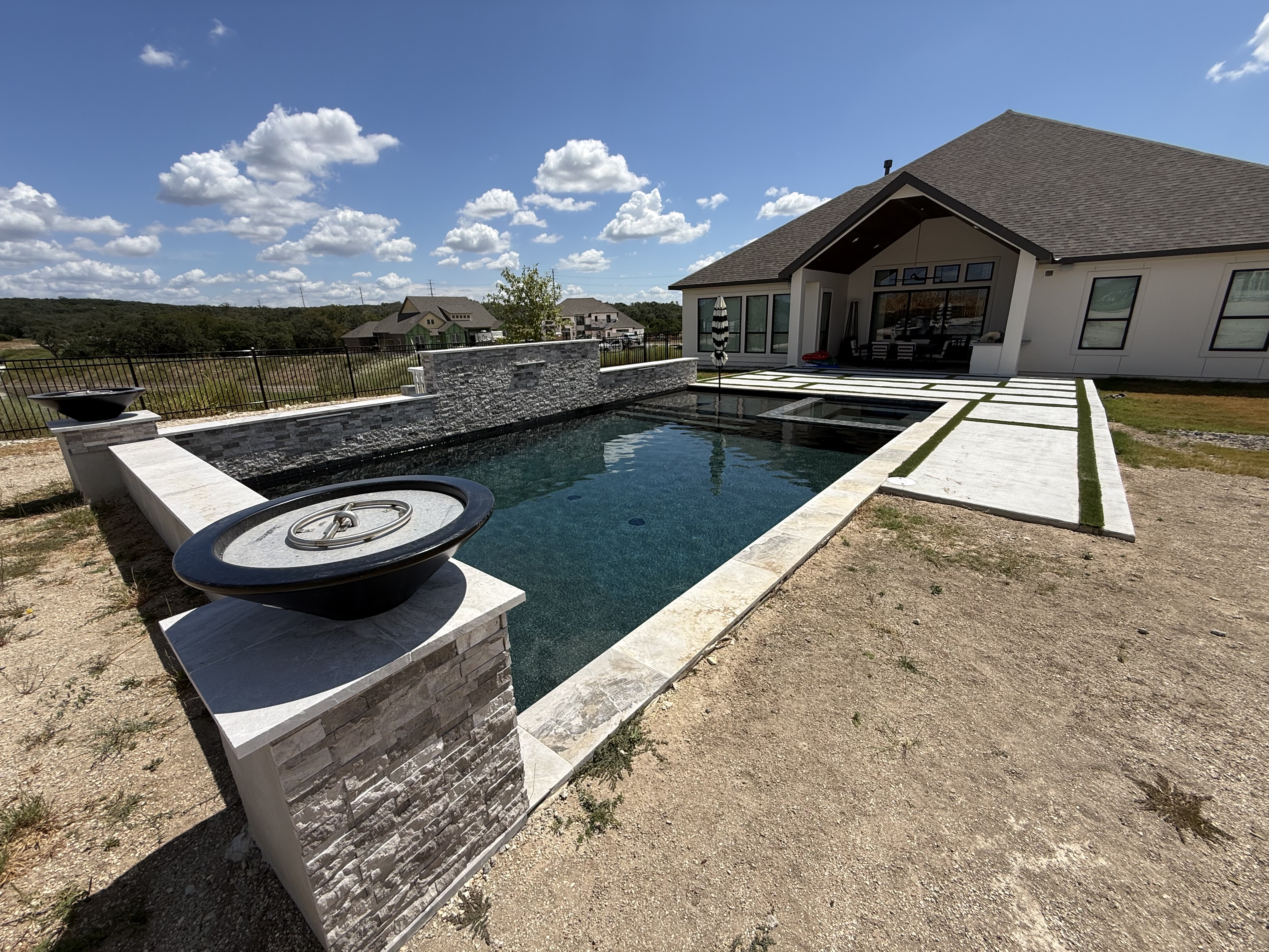 Boerne pool with light stone coping, built-in spa, stacked-stone waterfall wall and twin fire bowls overlooking the hills