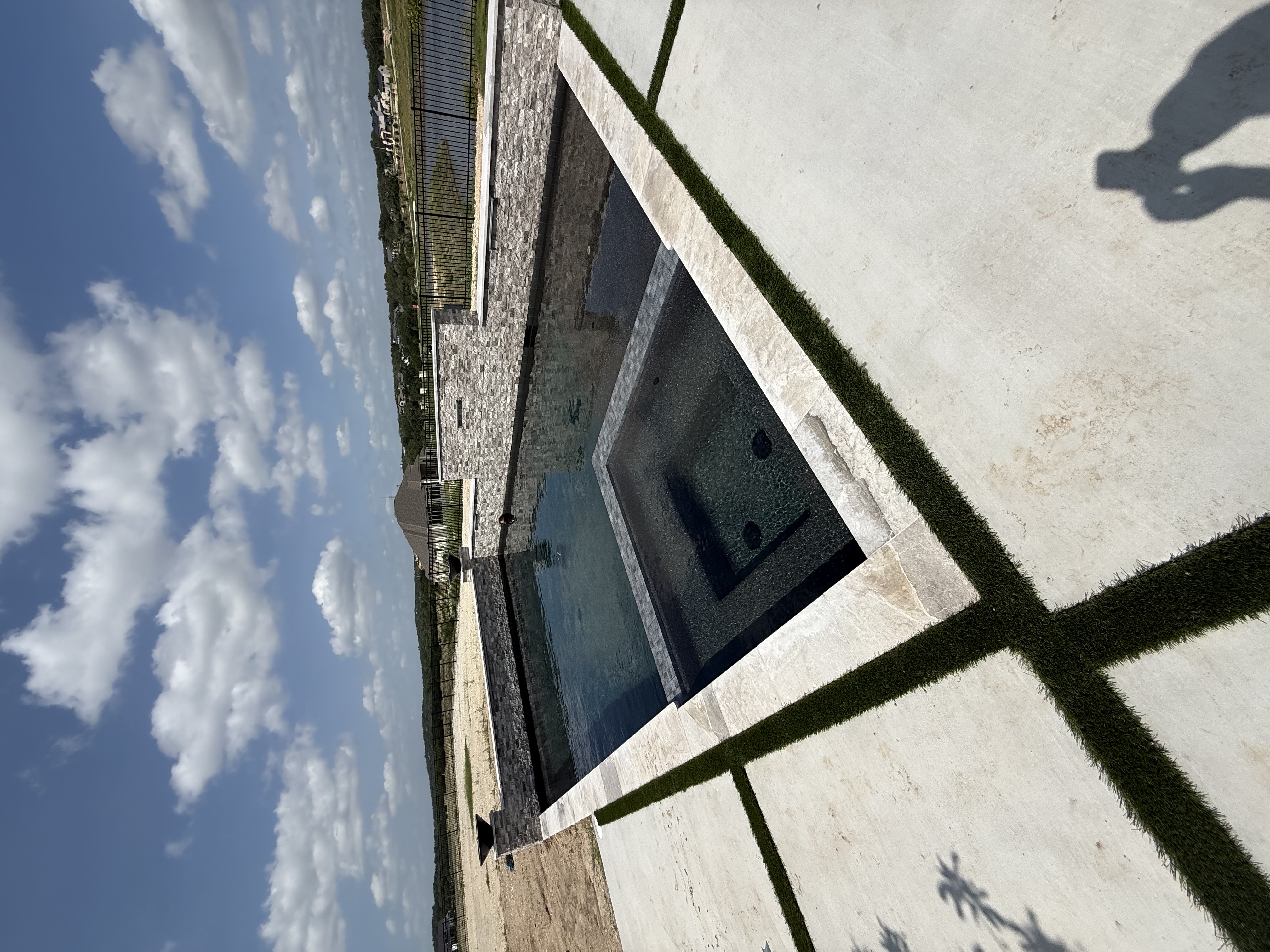 Boerne rectangular pool with an integrated square spa and stacked stone wall beside pavers with turf strips