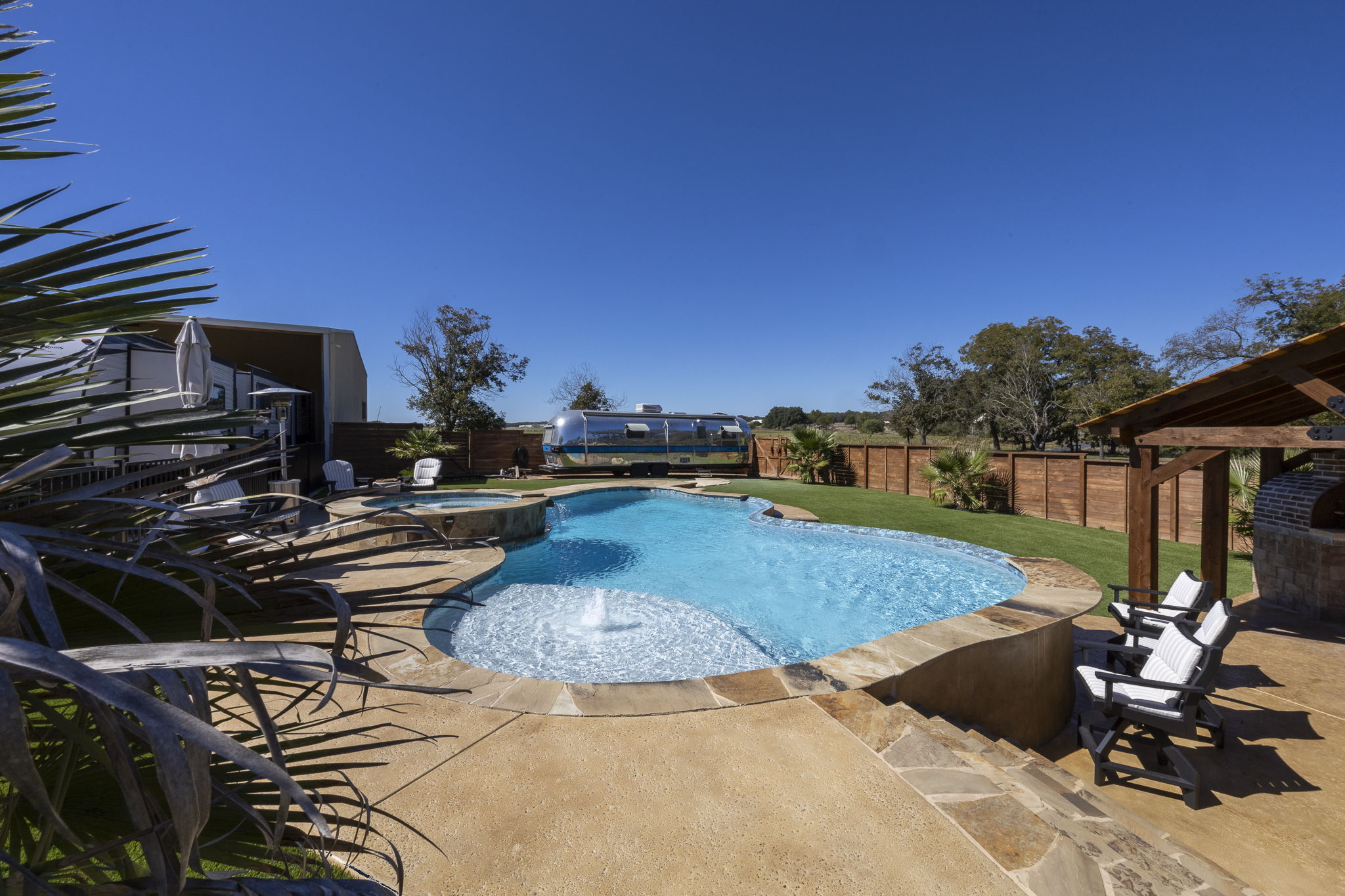 Comfort freeform pool at dusk with an elevated stone spa, sun shelf fountain, flagstone coping and blue waterline tile beside a small fire pit