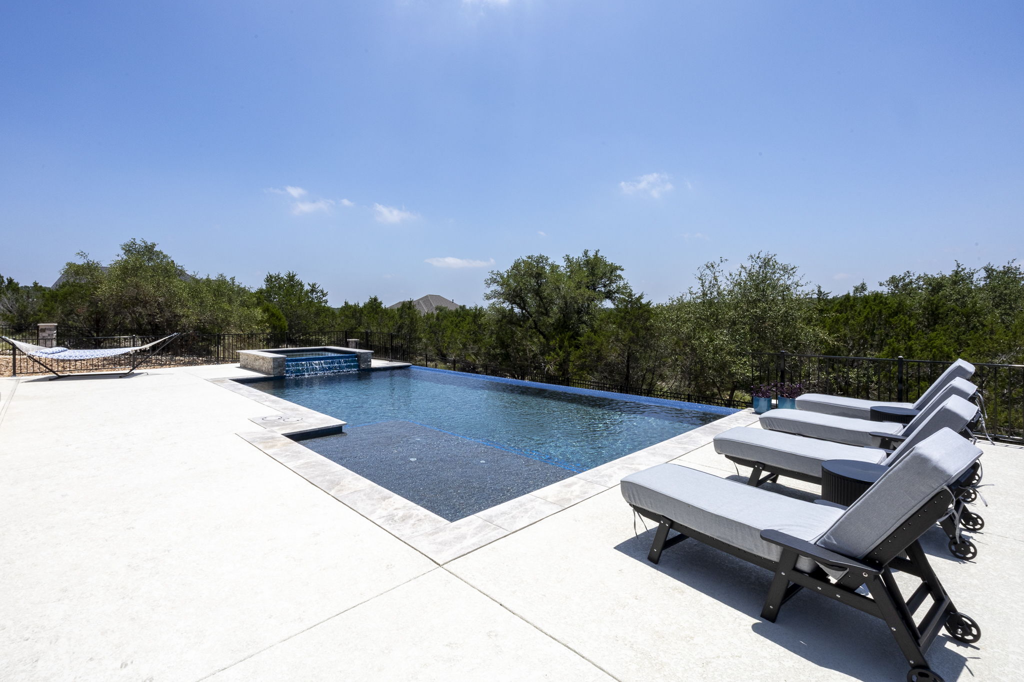 New Braunfels infinity-edge pool with sun shelf, raised hot tub waterfall and gray lounge chairs