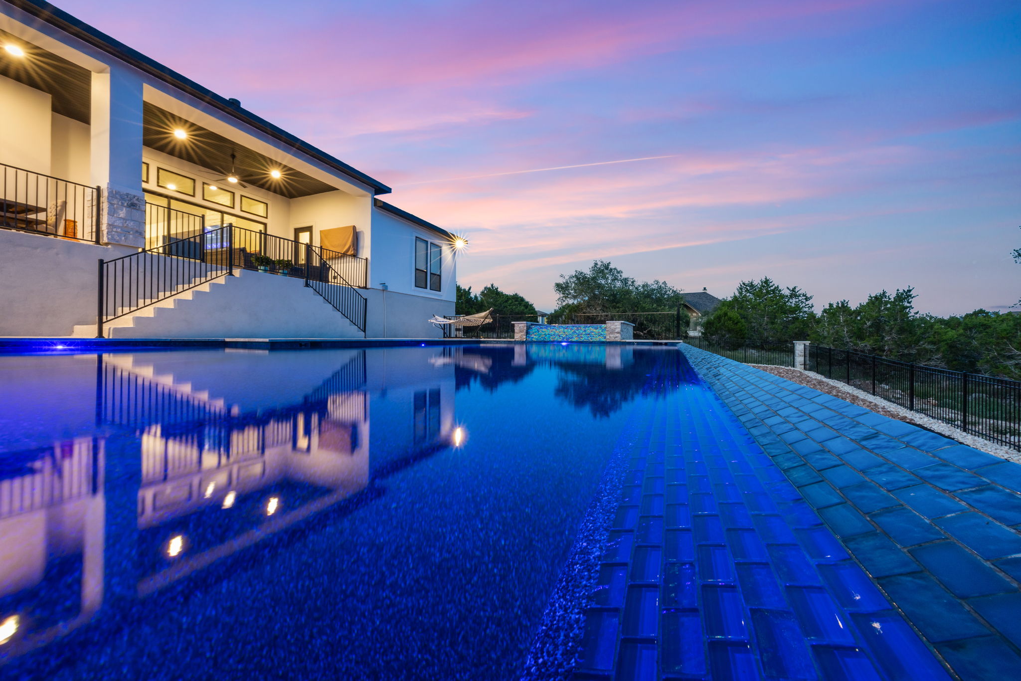New Braunfels twilight infinity-edge pool reflecting the modern home and sunset sky