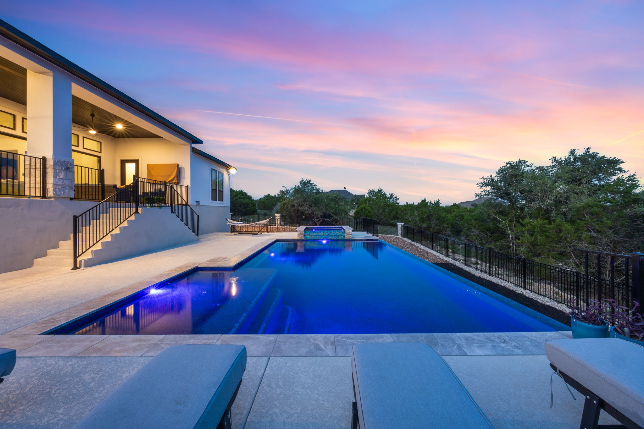 New Braunfels pool with built-in spa and shallow entry glowing at sunset beside a stone-accent home