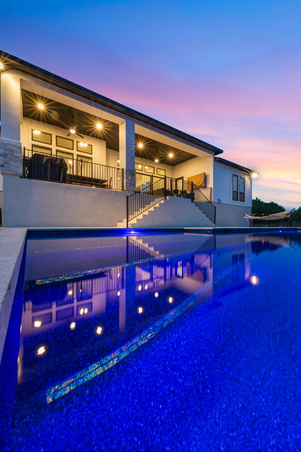 New Braunfels pool at dusk beside a covered patio supported by white pillars with an outdoor grill