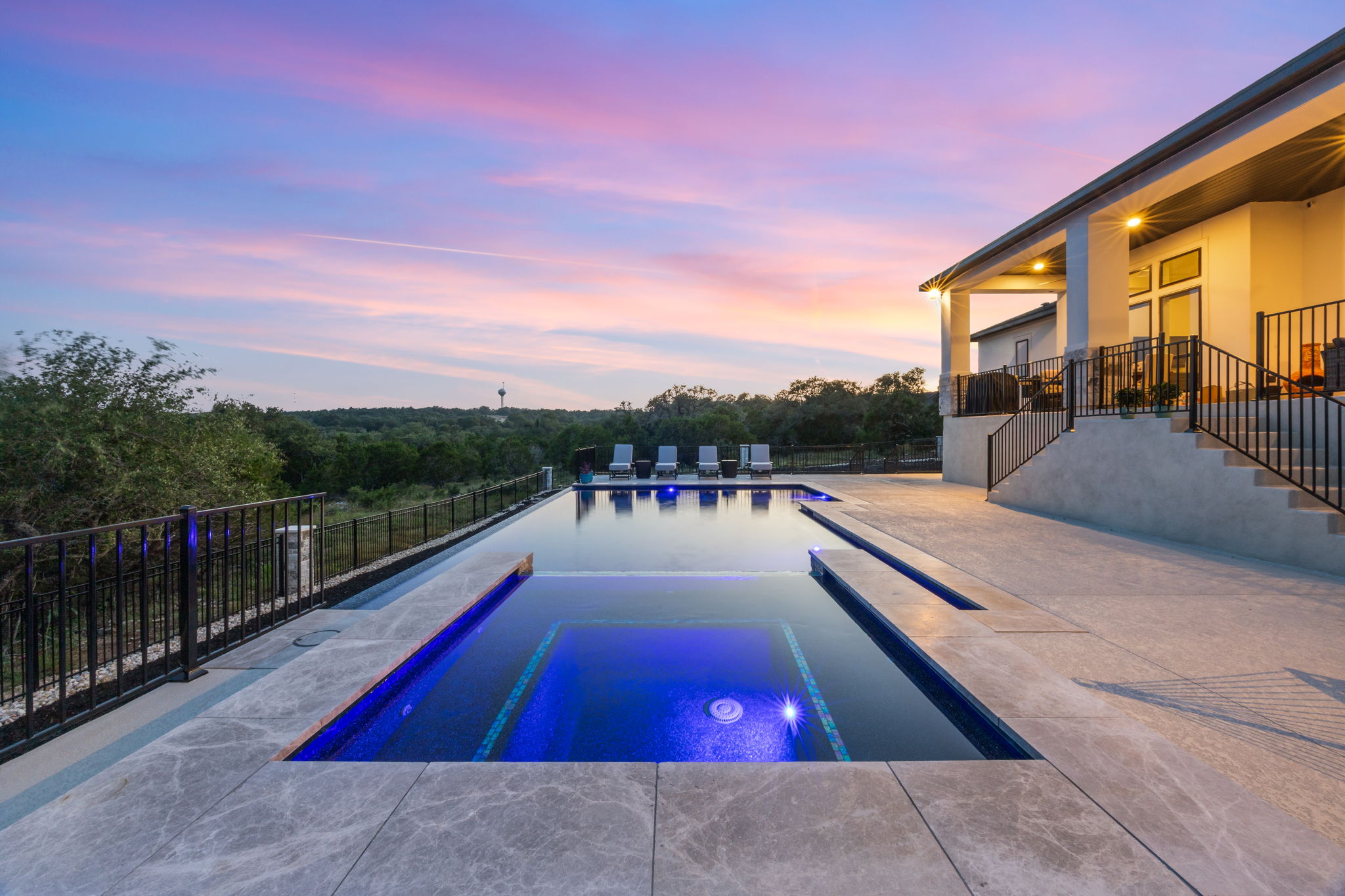 New Braunfels infinity-edge pool with an integrated illuminated spa at sunset