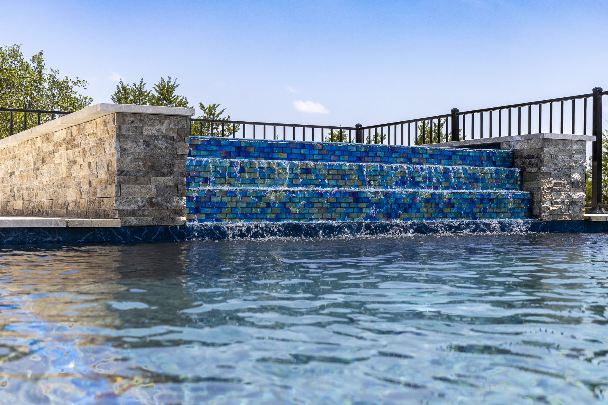 New Braunfels two-step pool waterfall with iridescent blue tiles framed by stacked stone pillars