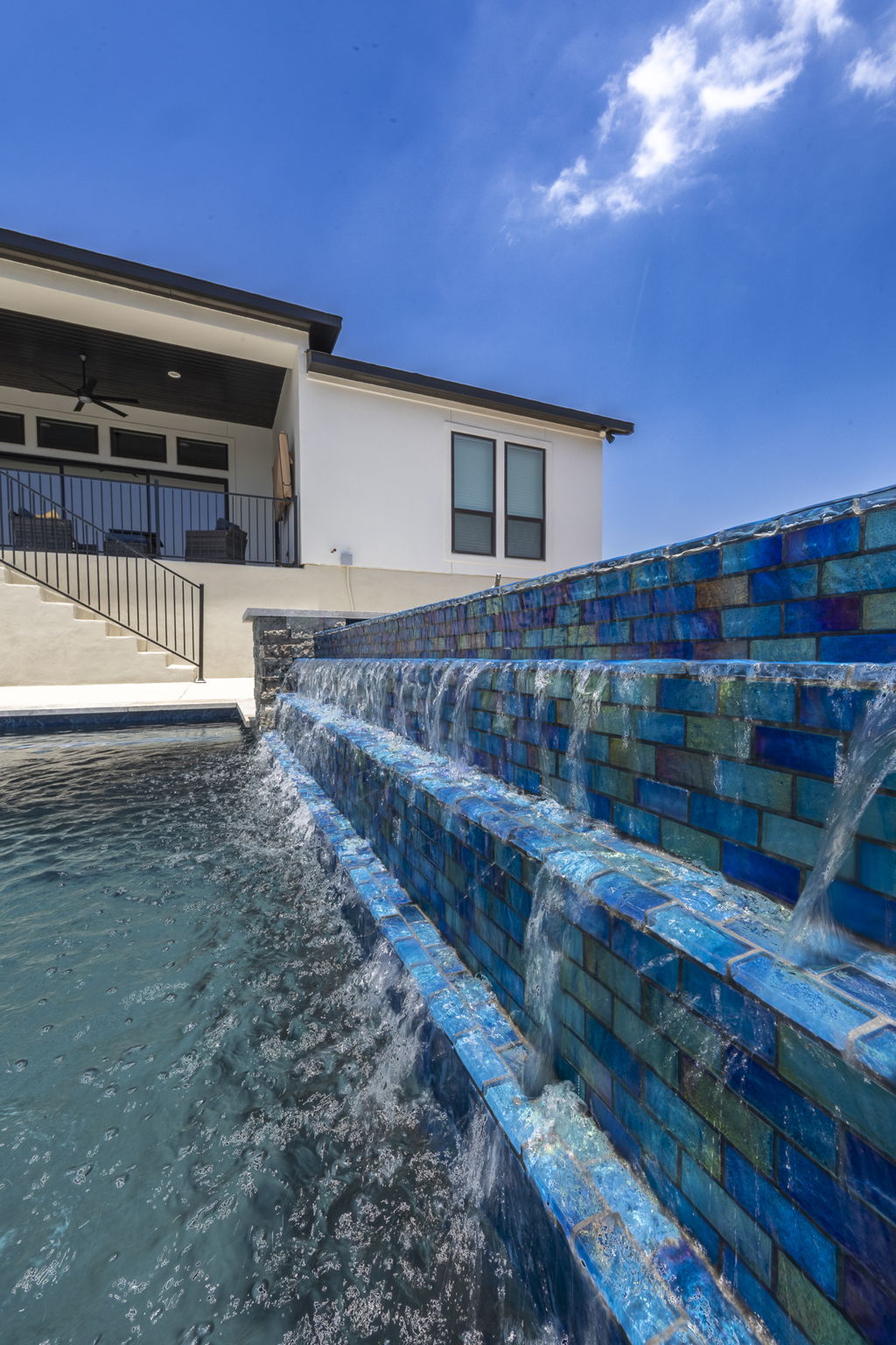 New Braunfels three-tiered pool waterfall with iridescent tiles beside the modern house balcony
