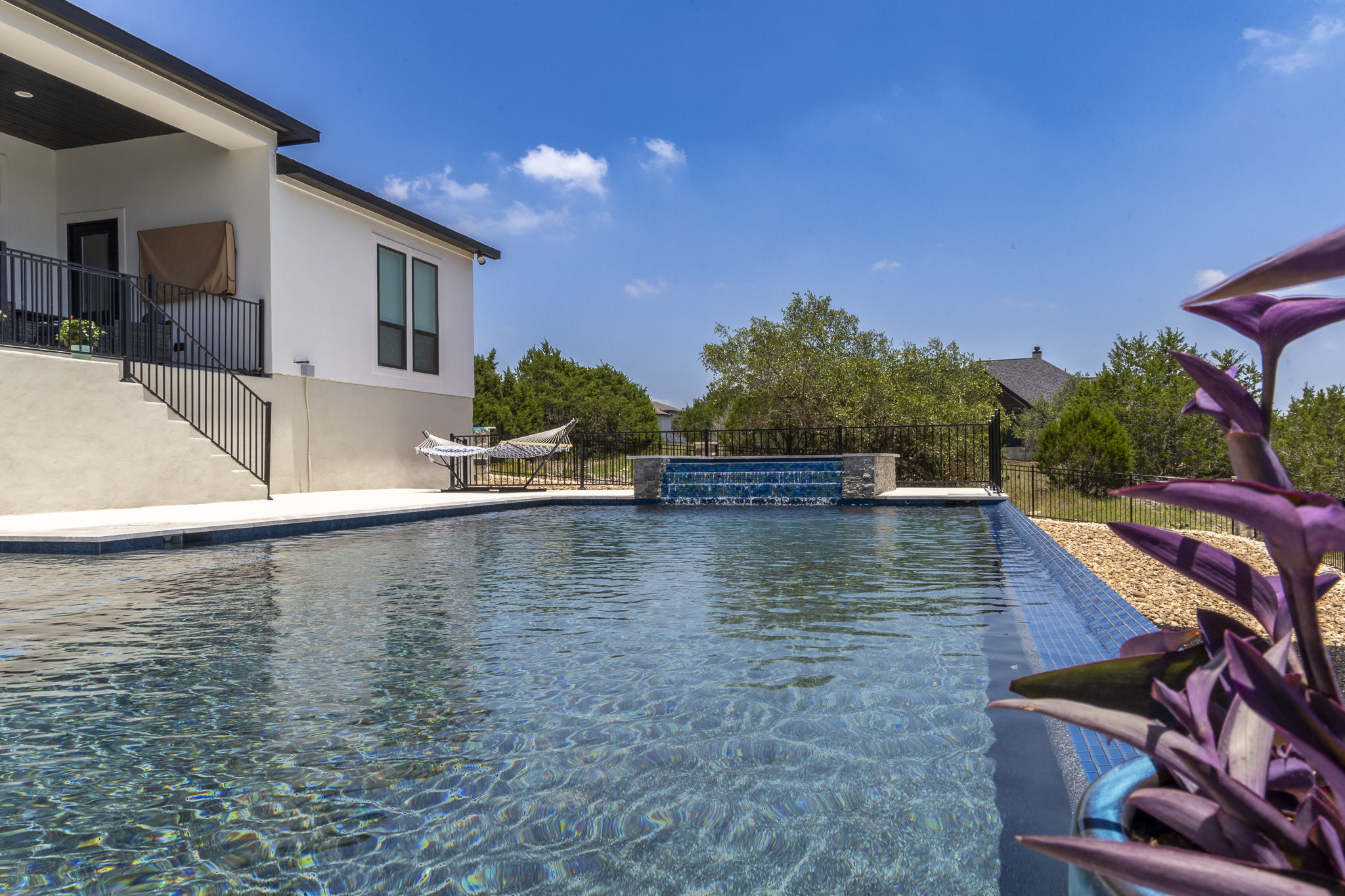 New Braunfels rectangular pool with a stone waterfall feature and infinity edge beside the two-story house