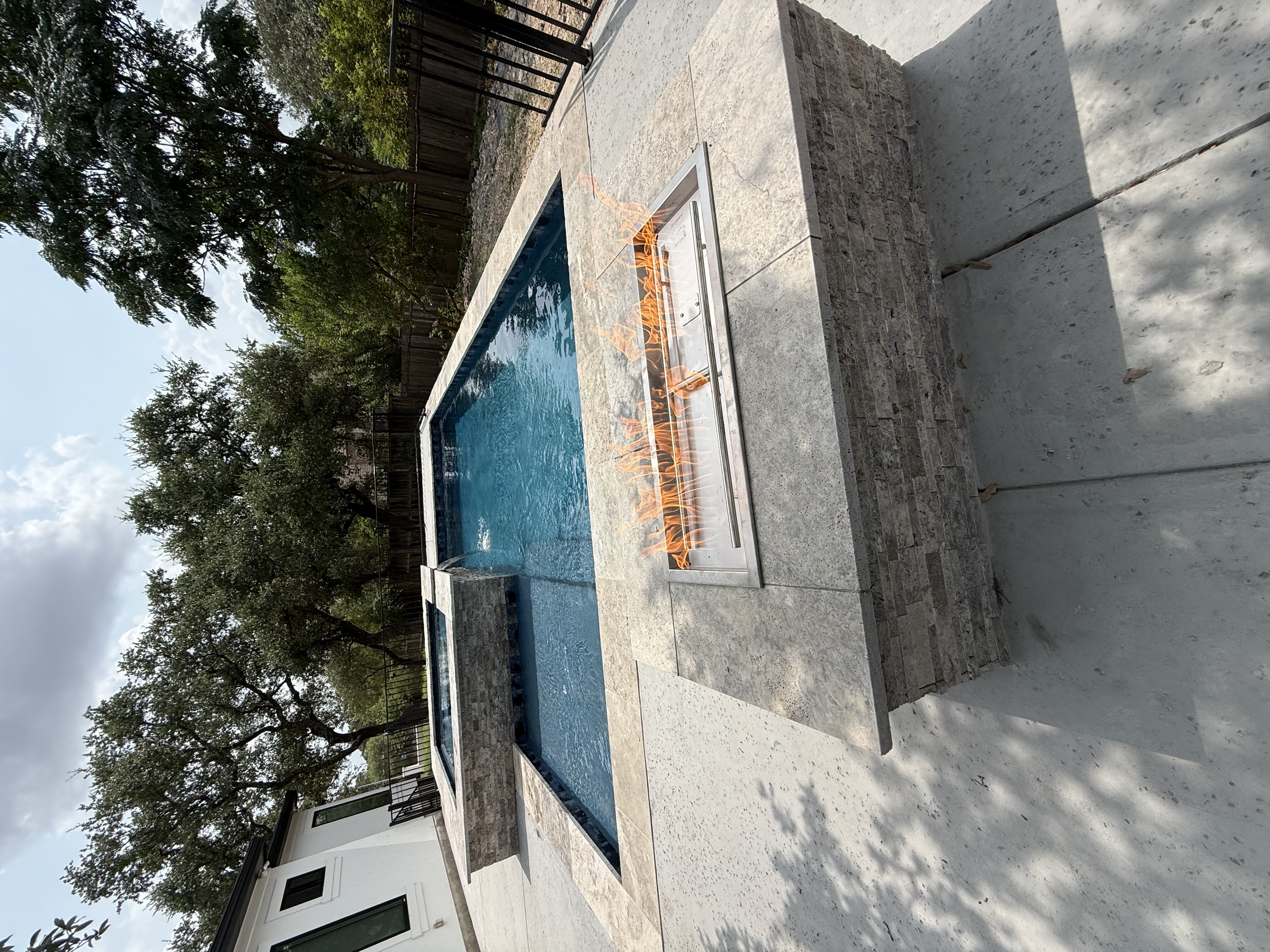 San Antonio pool with an elevated spa spillover and a linear fire pit built into a raised stone wall