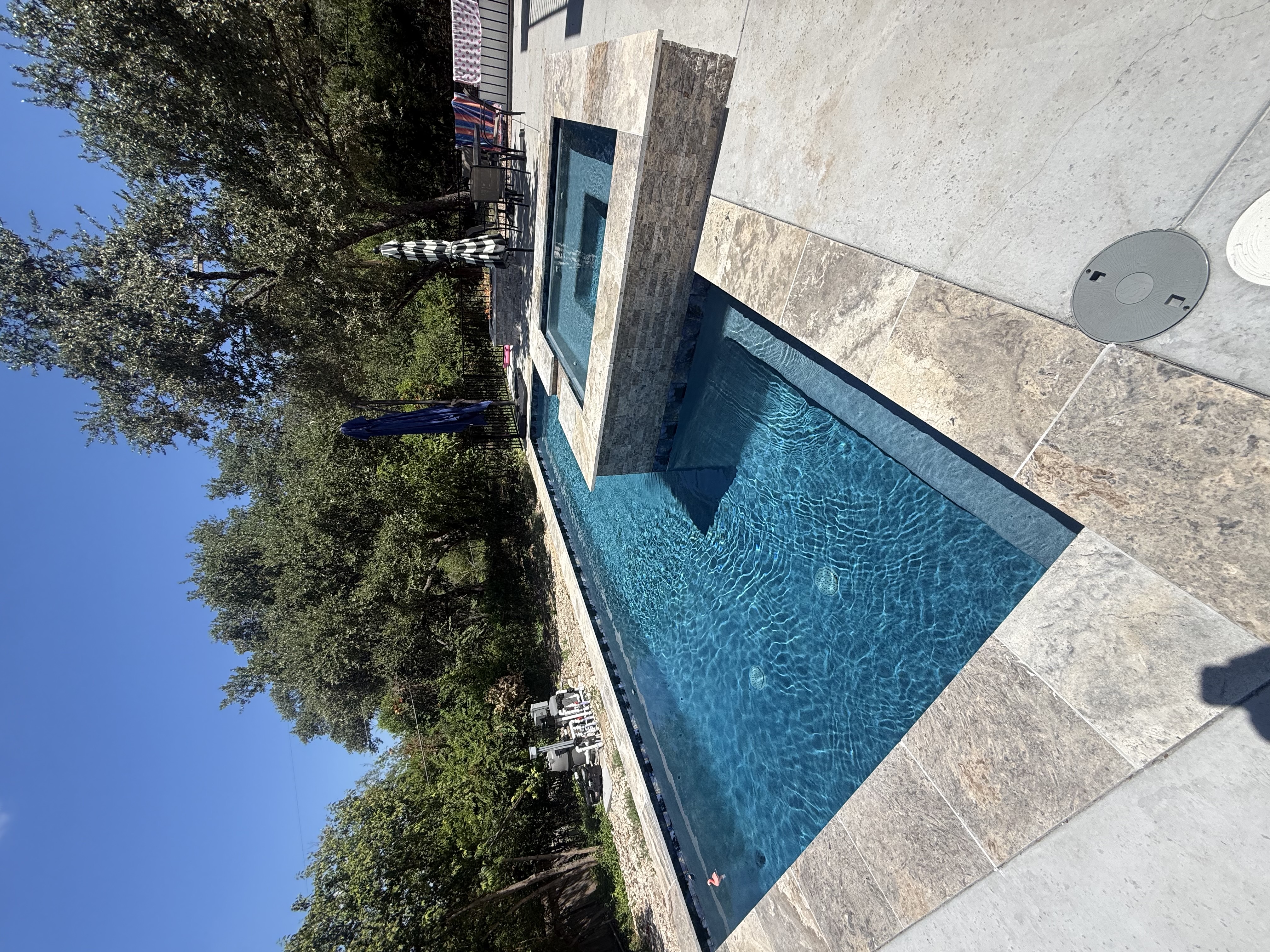 San Antonio pool with a raised stone-tiled spa spillover and a large stone tile patio with shade umbrellas