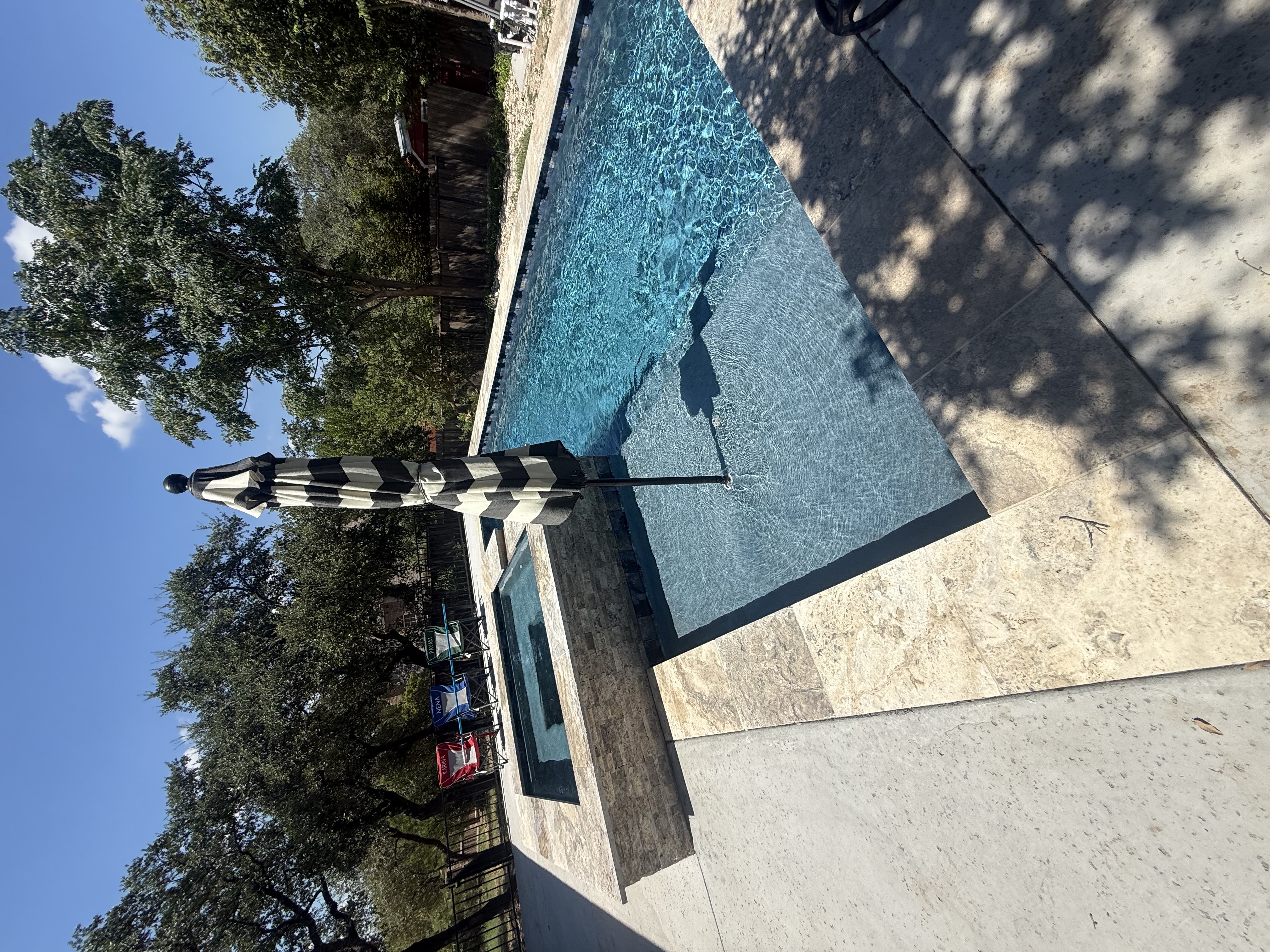 San Antonio pool with a tanning ledge under a striped umbrella and a stone-tiled hot tub