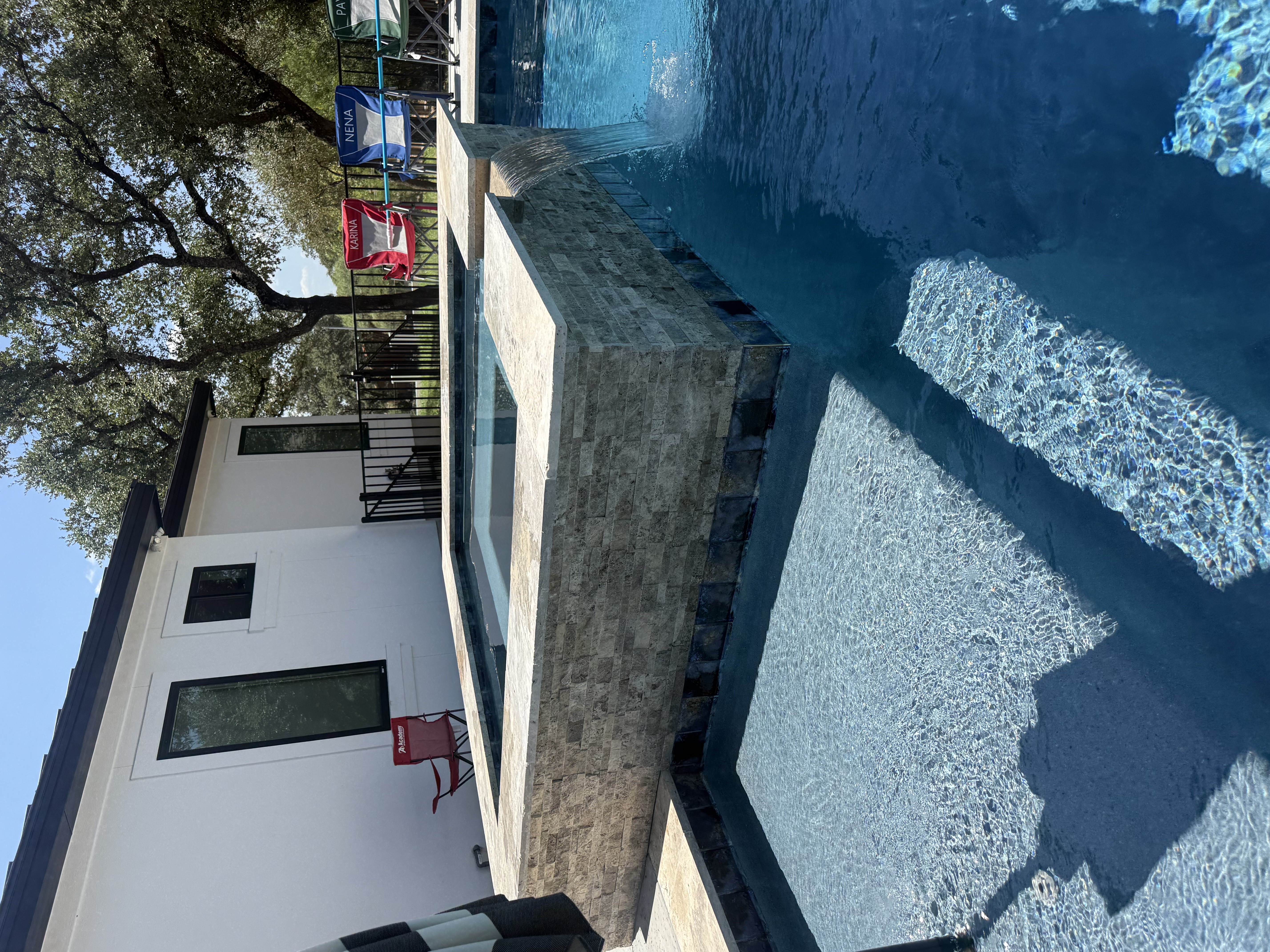 San Antonio pool with a raised stacked-stone hot tub waterfall spilling into the pool beside the house