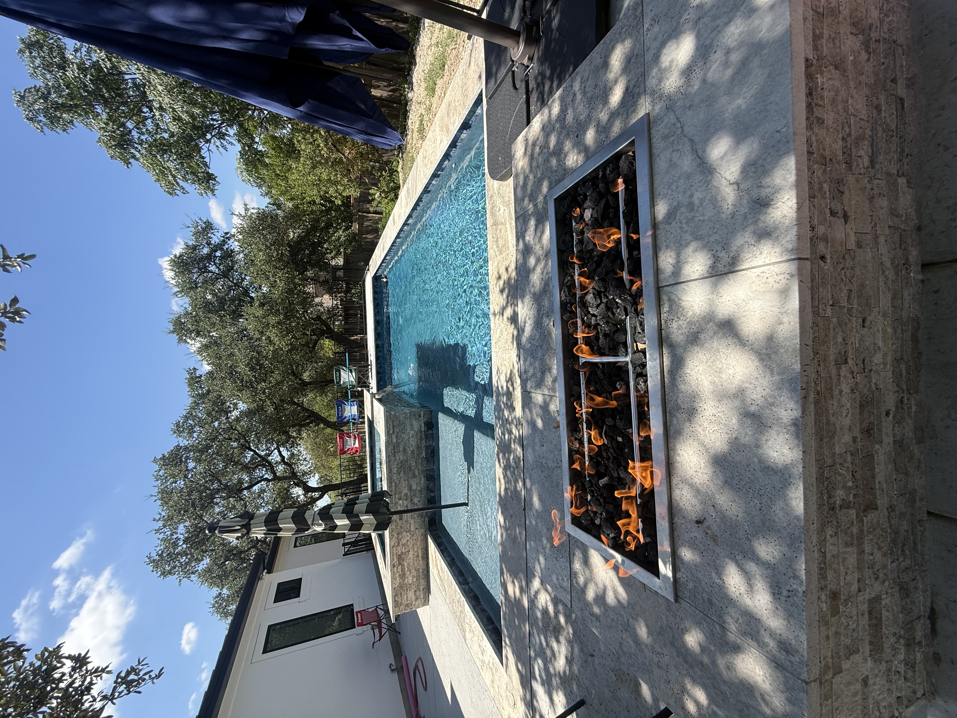 San Antonio gas fire pit with lava rock flames alongside a rectangular pool and square spa