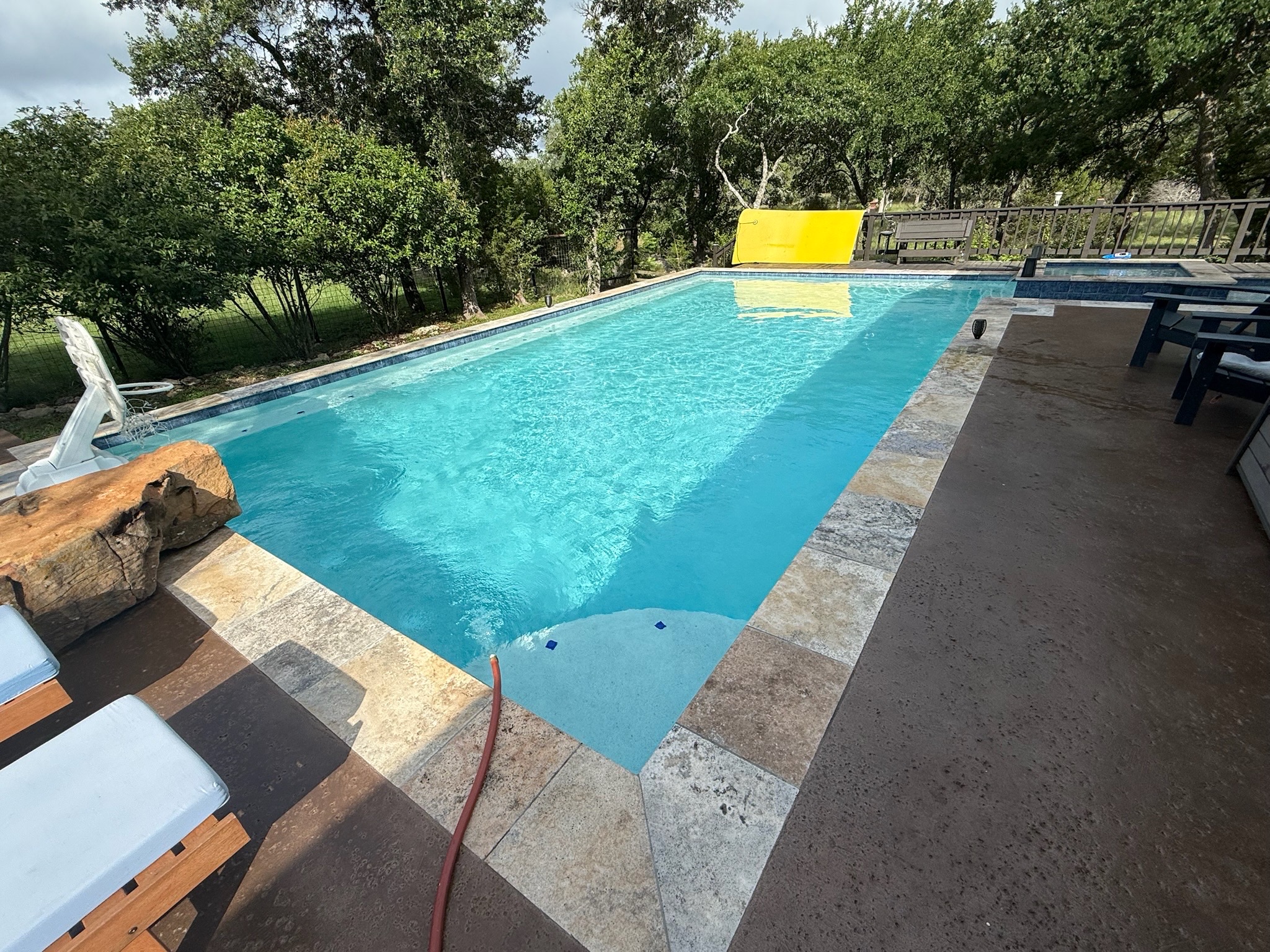 Spring Branch pool with sun shelf and stone coping in a wooded backyard